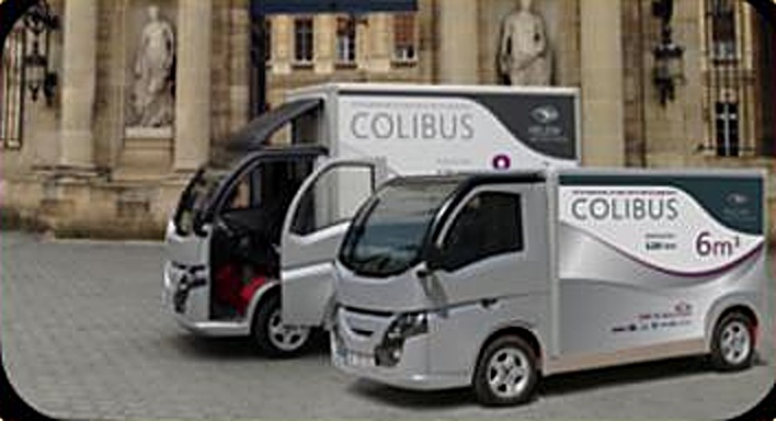 Deux utilitaires électriques Colibus devant une façade en pierre