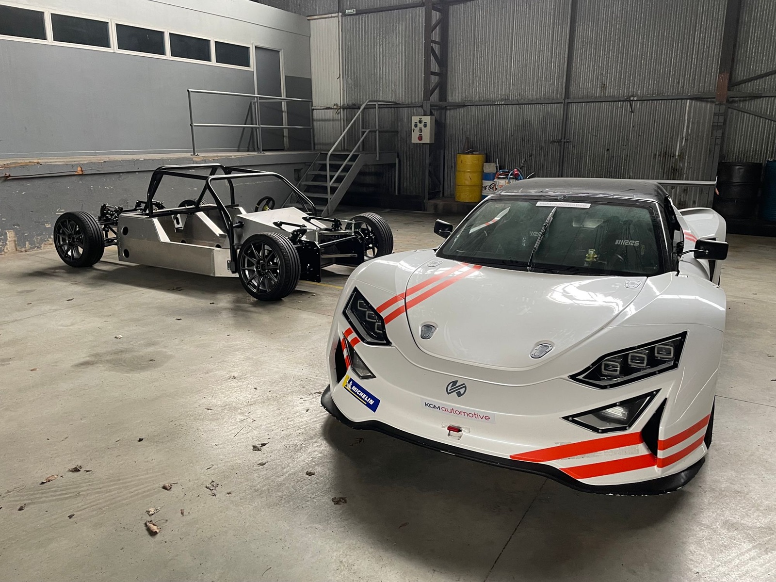 Châssis roulant et voiture carrossée, blanche à bandes orange, côte à côte dans un atelier
